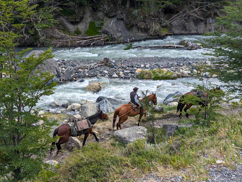 A gaucho on horseback next to the river in Windy Pass taking supplies up to the camps in Torres Del Paine National Park