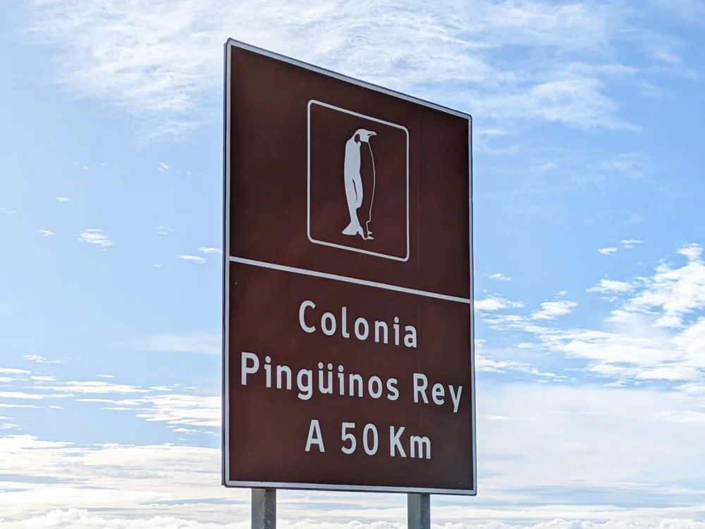 A brown road sign showing Colonia Pinguinos Rey is 50km away