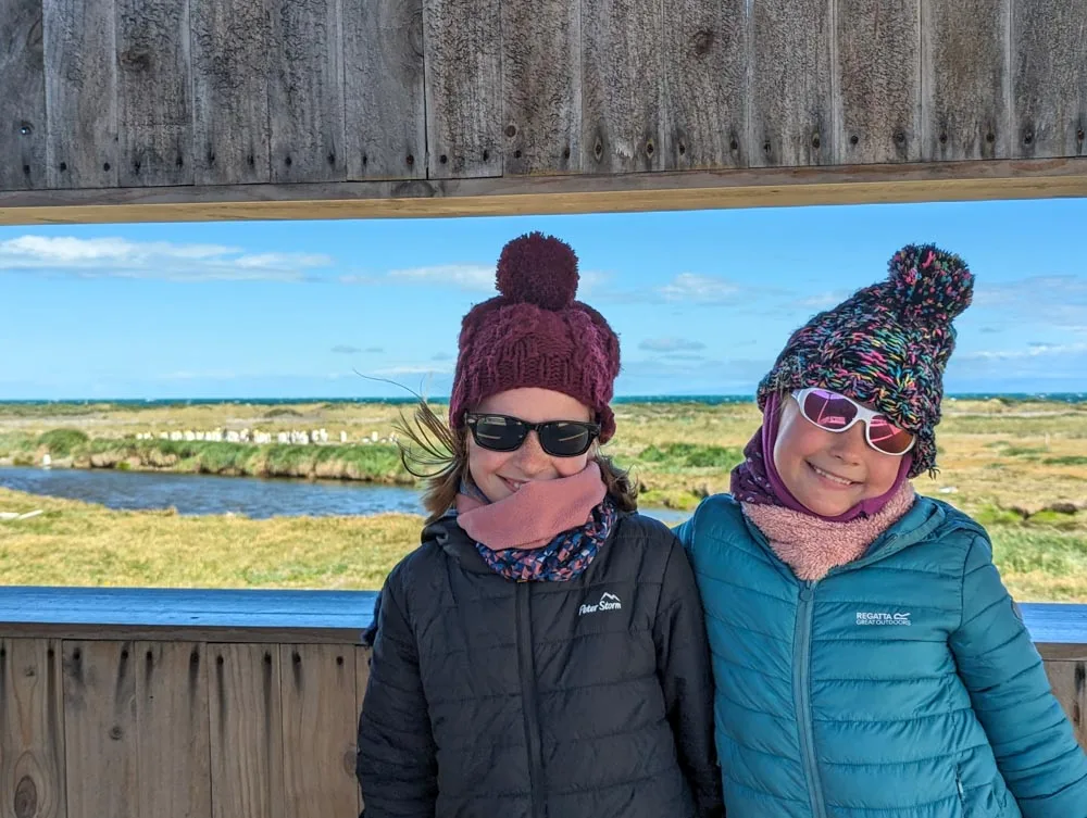 Georgia and Eva wrapped up warm in the viewing shelter at Park Pinguino Rey with the colony of king penguins in the background