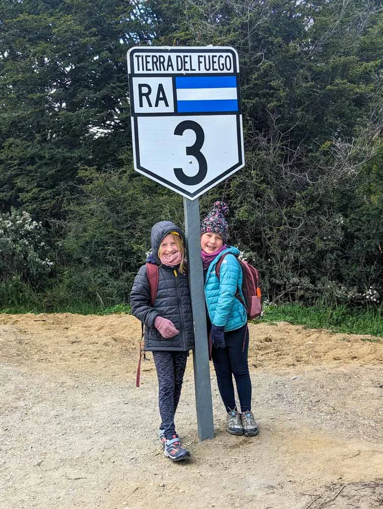 Georgia and Eva underneath a large Ruta 3 sign which marks the end of the road in Ushuaia.