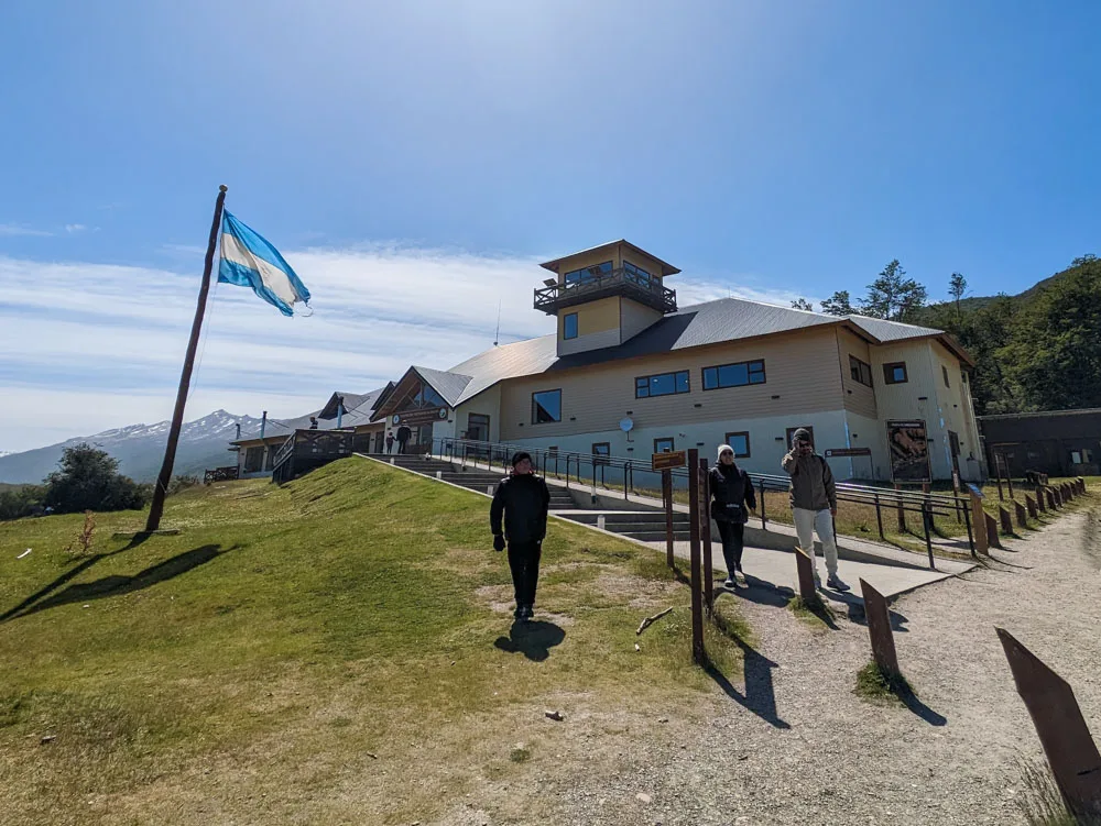 People walking away from Alakush Visitors Centre in Tierra del Fuego National Park with a large flag in front of the building.