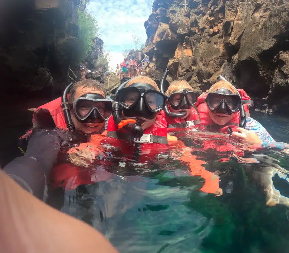 The Spencer family wearing life jackets, snorkels and masks in the water at Las Grietas on Santa Cruz Galapagos bay tour with kids.