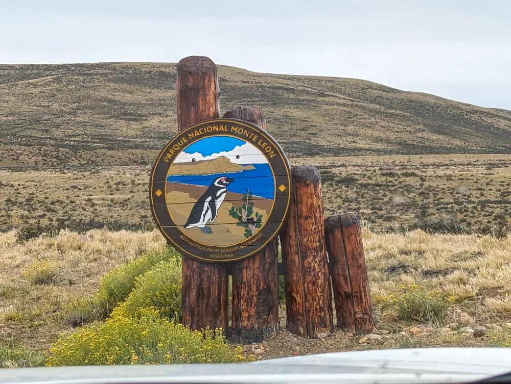A large sign for Monte Leon National Park showing a penguin on the beach next to the sea.