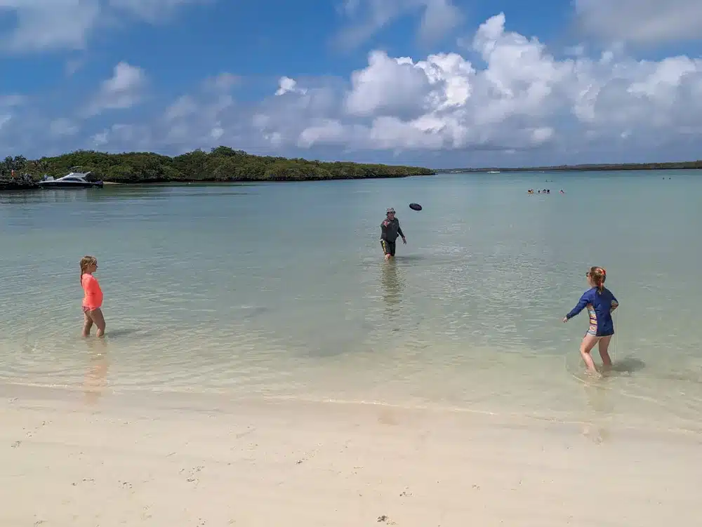 Adrian, Georgia and Eva playing a game of frisbee in the shallow waters of Tortuga bay. There are mangroves and a water taxi in the background.