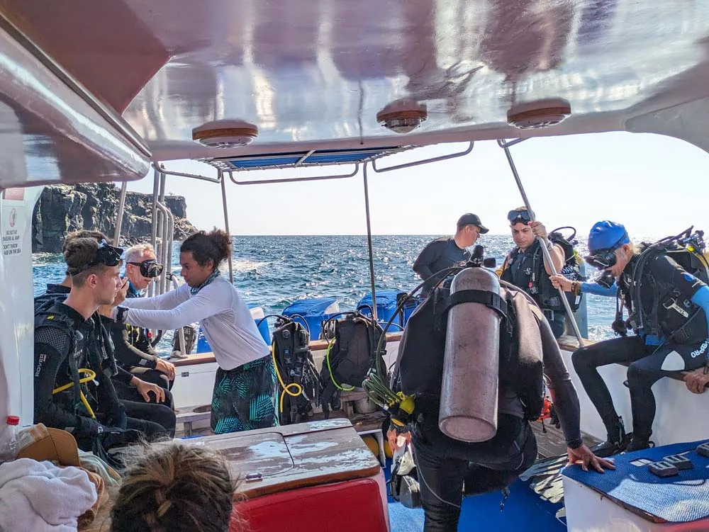 A group of divers getting their final gear on, sitting on the edge of the boat at the back at North Seymour Island Galapagos.
