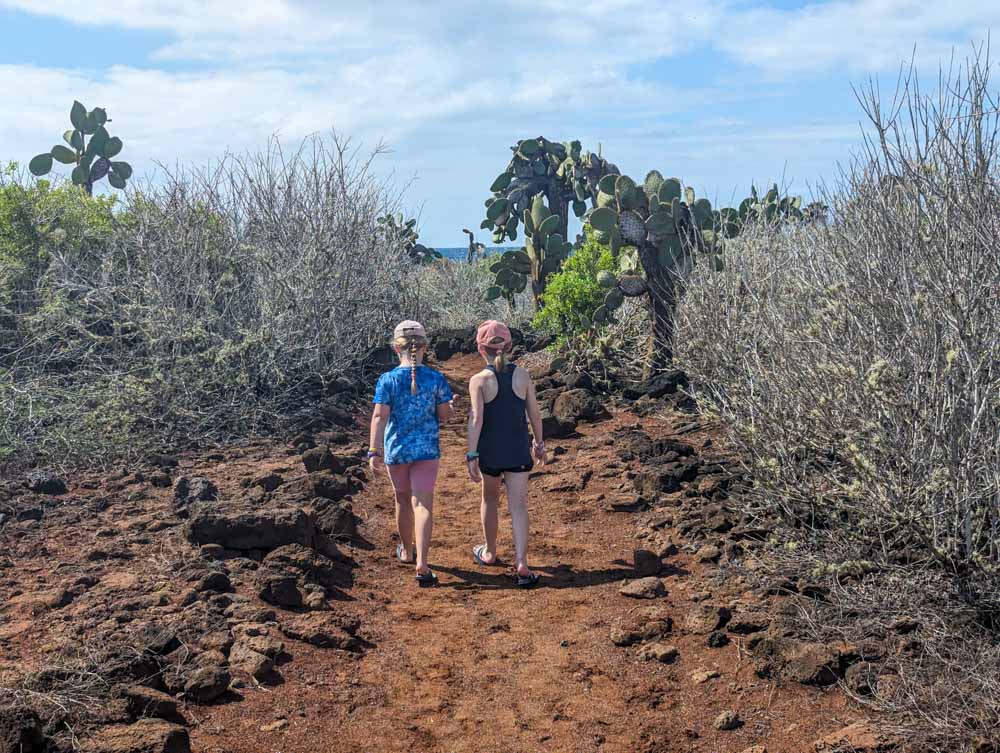 Georgia and Eva walking along the red sand path amongst bushes and cacti to Play De Los Perros.
