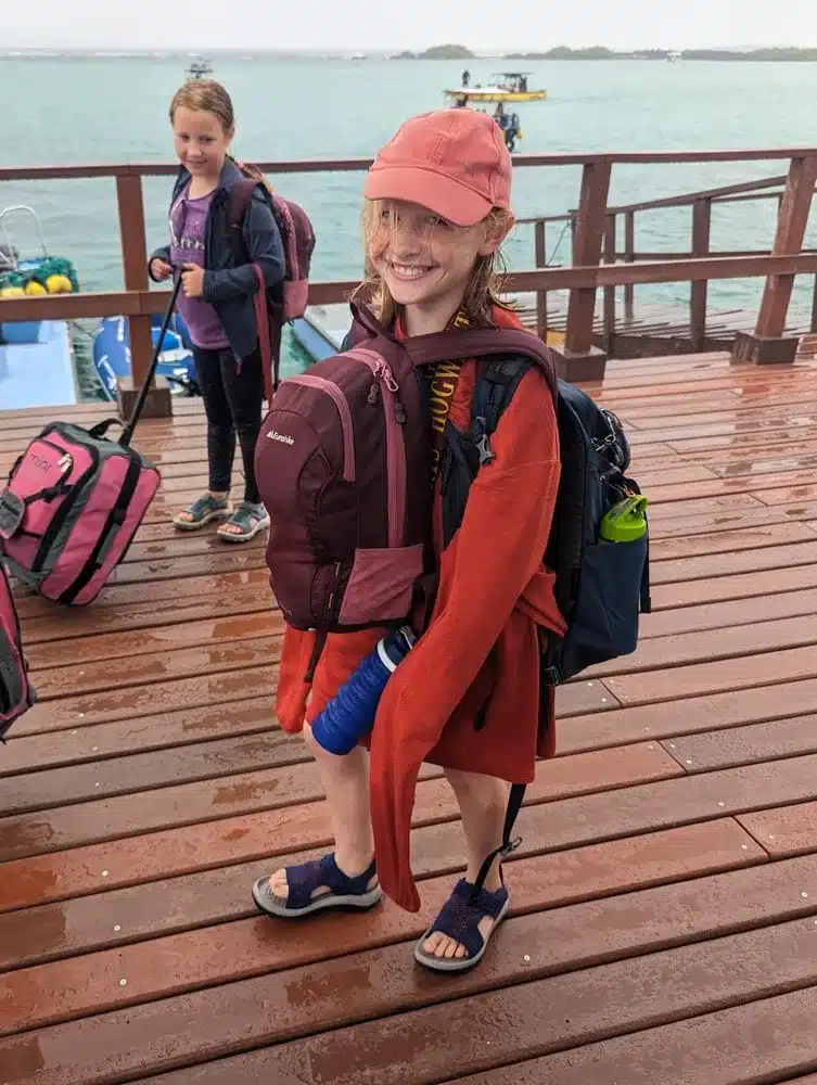 A wet but happy Georgia on the pier on Isla Isabella carrying a rucksack on her front and her back with Eva in the background with her luggage.