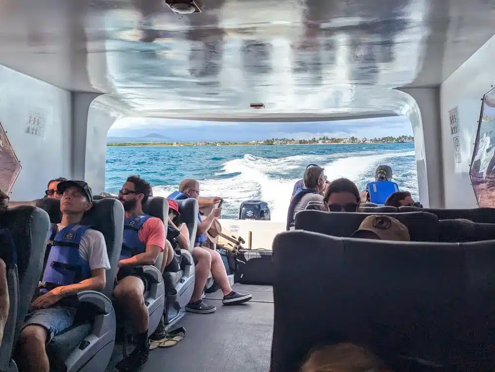 Looking back down the passenger ferry with passengers in their seats and Isla Isabella in the distance as the boat powers through the water.